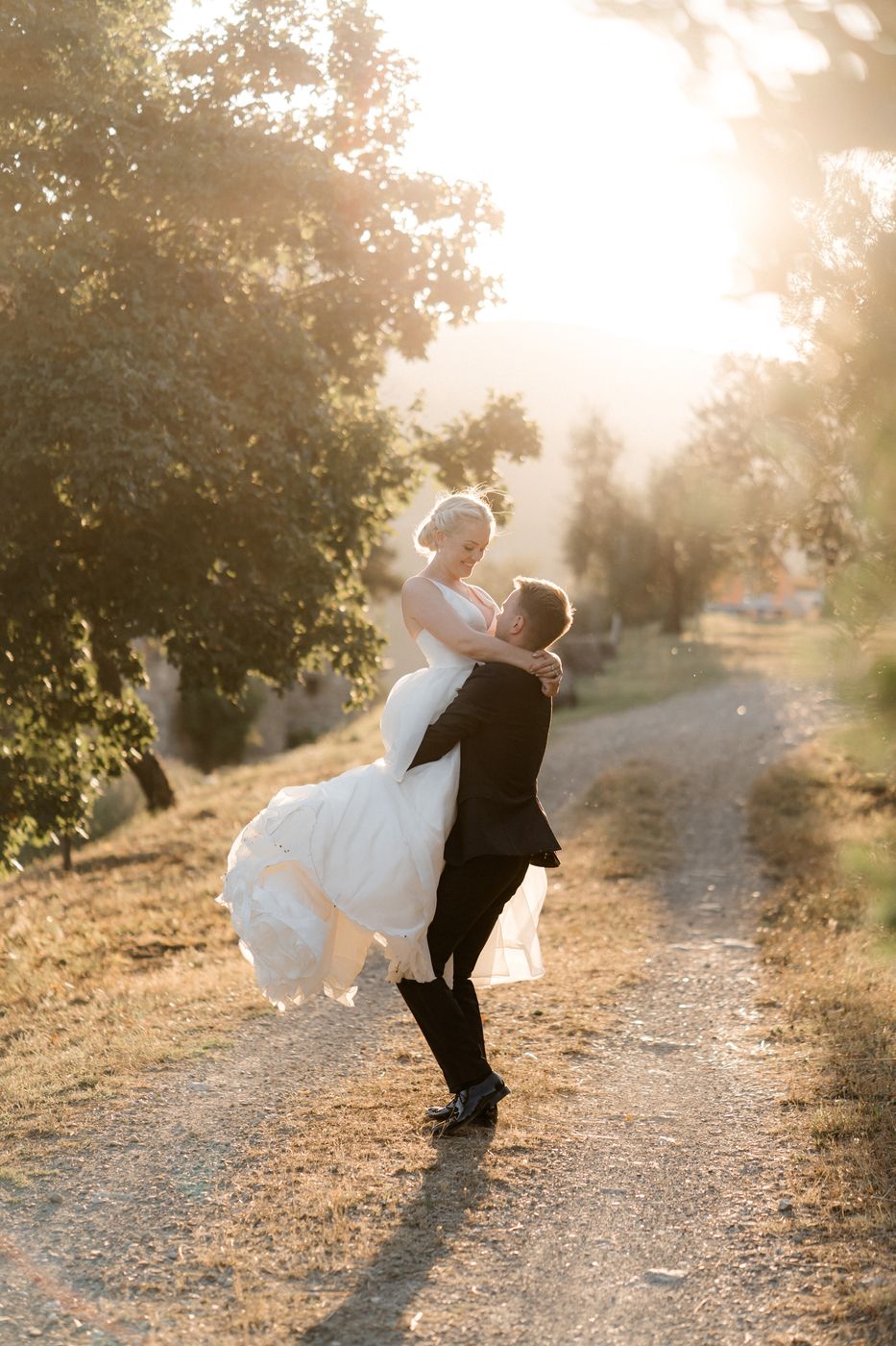 Lo sposo solleva la sposa su una strada sterrata al tramonto