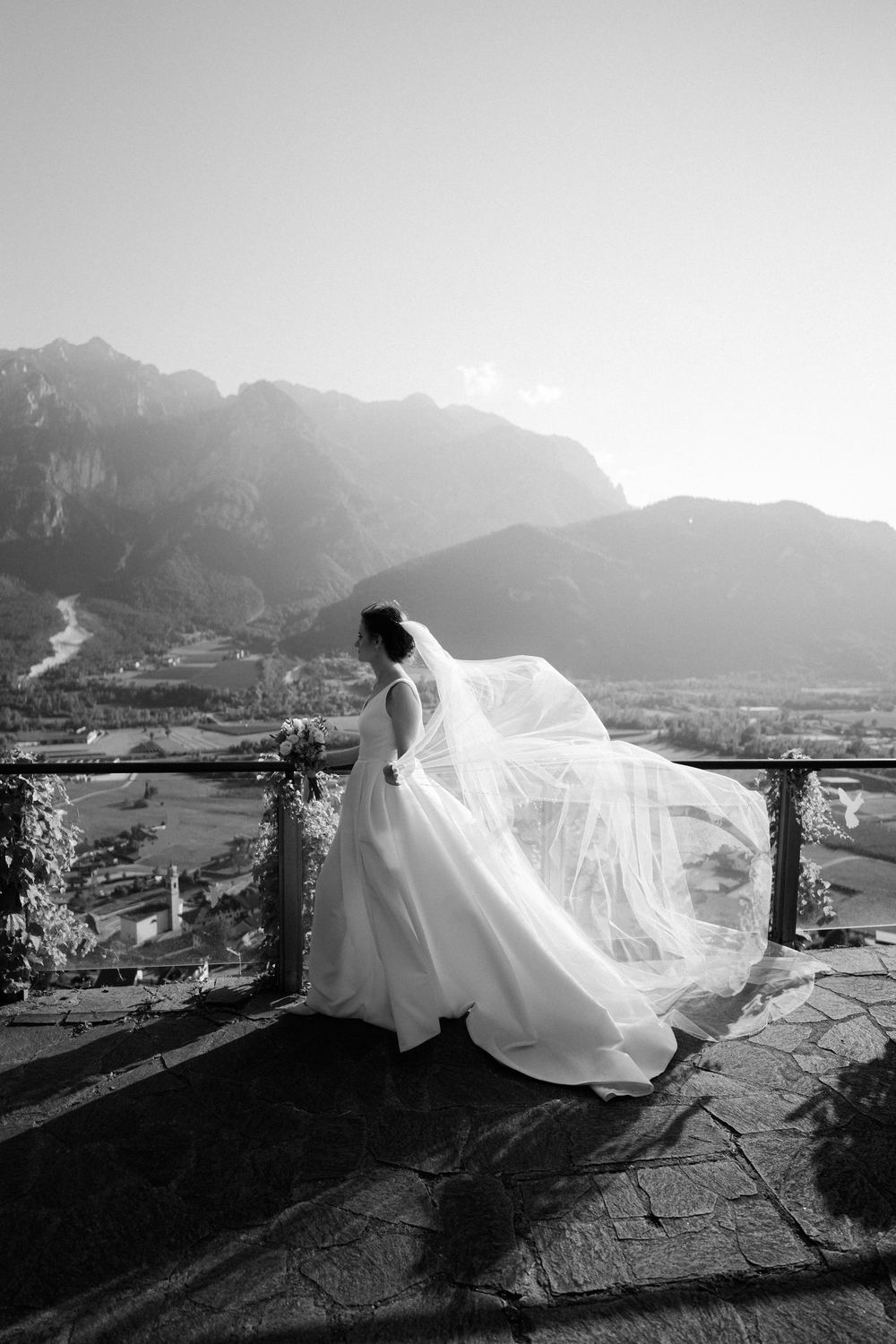 Sposa in bianco e nero sulla terrazza, il velo nel vento e le montagne dietro
